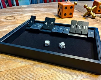 May include: A black wooden game tray with a black felt lining. The tray has a row of numbered tiles from 1 to 12. Two white dice are on the felt.