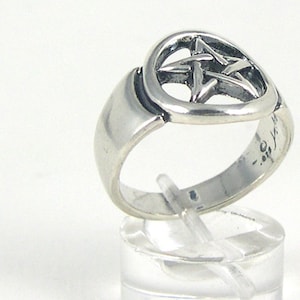 Peut inclure: Une bague en argent avec un motif de pentagramme. La bague est sur un présentoir transparent.