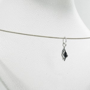 Op de afbeelding: Een zilverkleurige ketting met een kleine, abstracte hanger. De hanger heeft een donker interieur en een vloeiende, organische vorm. De ketting wordt gepresenteerd tegen een witte achtergrond, waardoor het ontwerp en de details van de sieraden worden benadrukt.