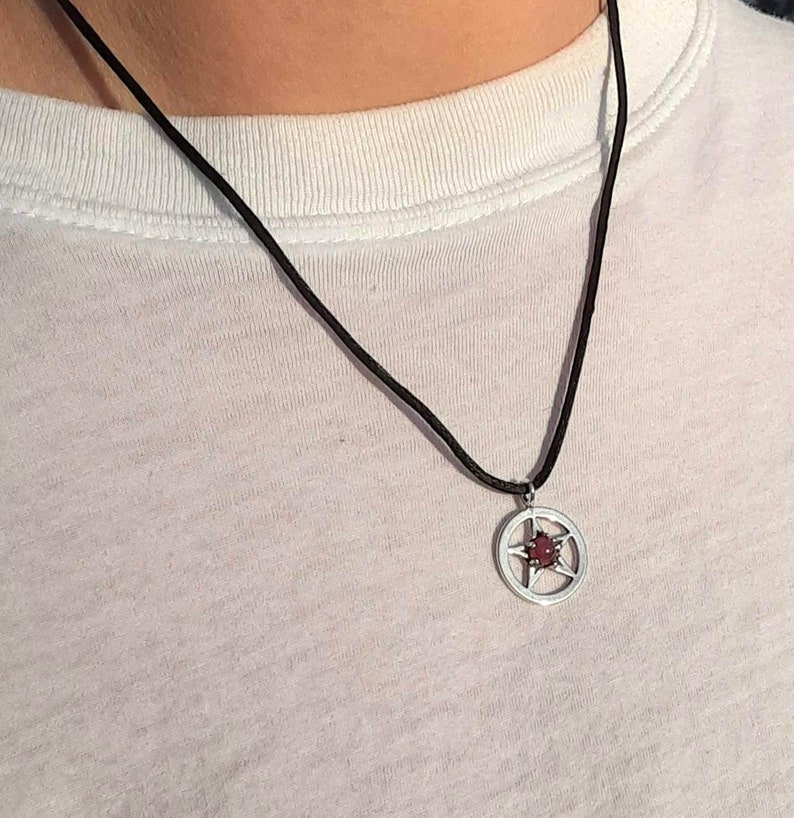 May include: A black cord necklace with a silver pendant featuring a five-pointed star with a red centre.