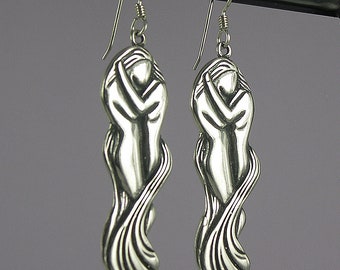 May include: Sterling silver earrings featuring a pair of figures embracing each other. The figures are stylized and abstract, with flowing lines and curves. The earrings are a unique and romantic piece of jewelry.