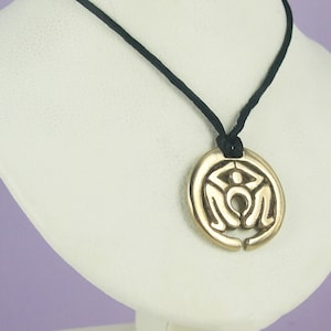 May include: Gold pendant necklace with a circular design featuring the word "MOM" in a stylised font. The necklace is on a black cord.