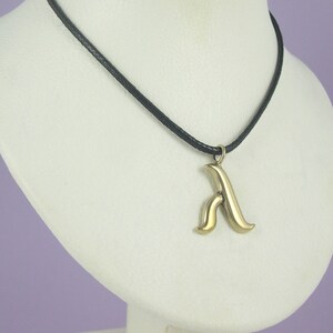 May include: A gold pendant necklace with a stylised letter 'A' charm on a black cord.