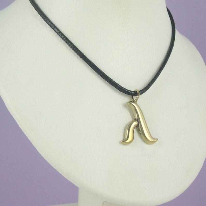 May include: A gold pendant necklace with a stylised letter 'A' charm on a black cord.