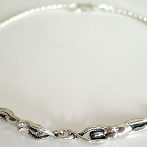 May include: Silver necklace with two abstract swimmer figures linked by a chain. The figures have a smooth, matte finish. The necklace is a unique piece of jewellery.