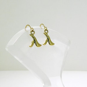 Puede incluir: Un par de pendientes de color dorado con un diseño abstracto único. Los pendientes están hechos de metal y tienen un estilo simple y elegante.