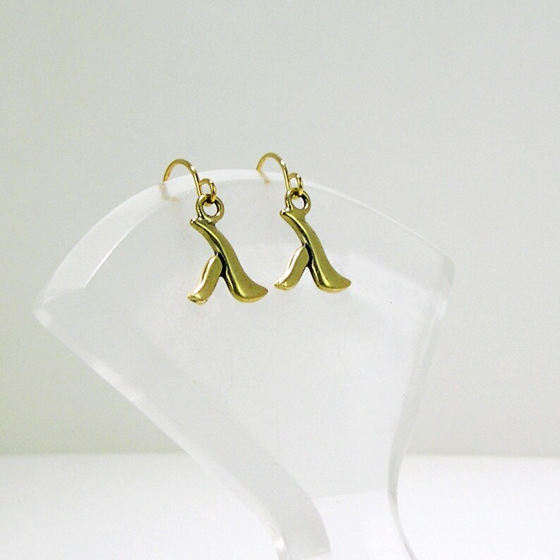 May include: A pair of gold-toned earrings with a unique abstract design. The earrings are made of metal and have a simple, elegant style.