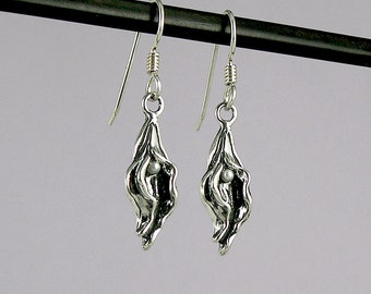 May include: A pair of silver dangle earrings with a textured, organic shape resembling a pod or a flower. Each earring features a small pearl bead inside the pod.
