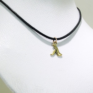Puede incluir: Un collar de cordón negro con un colgante de oro en forma de letra A estilizada.