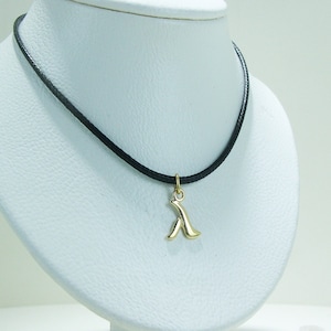 Puede incluir: Un collar de oro con un colgante de diseño abstracto estilizado que cuelga de un cordón negro.