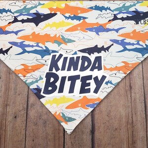 May include: White dog bandana with a blue shark pattern and the text "Kinda Bitey" in a blue circle.