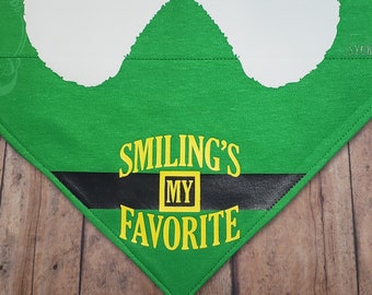 May include: Green dog bandana with a white elf hat design and the text "Smiling's My Favorite" in yellow letters.