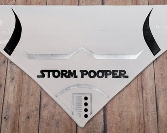 May include: White dog bandana with a black and silver Stormtrooper design. The bandana has the text "STORM POOPER" printed on it.