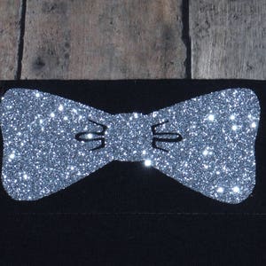May include: A silver glitter bow tie design on a black fabric background.
