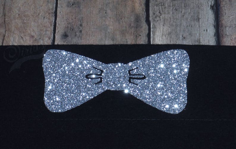 May include: A silver glitter bow tie design on a black fabric background.