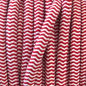 Può includere: Primo piano di una bobina di corda a motivo chevron rosso e bianco. La corda è avvolta strettamente, con il motivo rosso e bianco che crea un design a zig-zag. La trama della corda è visibile, suggerendo un materiale resistente.