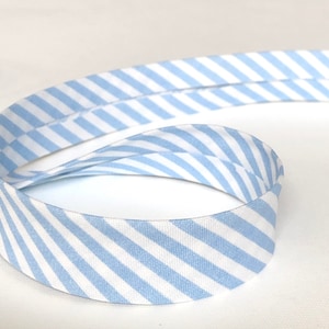 Peut inclure: Gros plan sur un ruban à rayures bleu clair et blanc, enroulé en spirale. Le ruban présente un motif à rayures diagonales et est fait d'un matériau doux et tissé. Le fond est blanc uni.