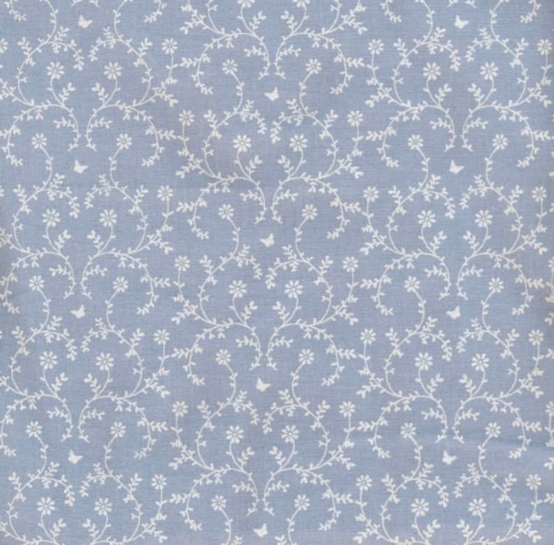 May include: A light blue fabric with a repeating pattern of white floral vines and small butterflies. The design features delicate white flowers and leaves, creating a soft, elegant aesthetic. The overall look is reminiscent of a vintage or cottagecore style.