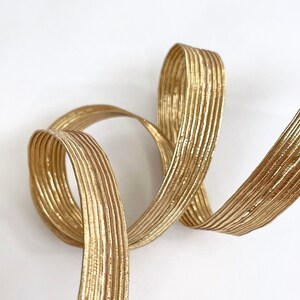 Peut inclure: Un ruban doré enroulé et bouclé sur fond blanc. Le ruban présente une surface texturée et côtelée, et l'éclat métallique capte la lumière. Ce ruban décoratif est adapté aux travaux manuels et à l'emballage de cadeaux.