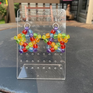 May include: A pair of handmade earrings featuring a starburst design. The earrings are crafted with small, colorful beads in a rainbow of hues, including red, orange, yellow, green, blue, and purple. The earrings hang from silver-colored hooks.