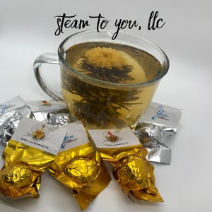 May include: Four gold foil-wrapped tea balls with labels that say "Womb Love Blooming Tea" and "Fertility Blooming Tea". A glass mug with a blooming tea flower in it. The text "steam to you, llc" is written in black cursive at the top of the image.
