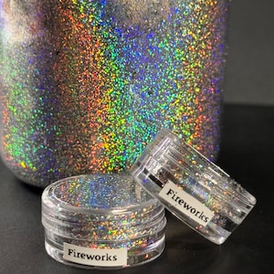 May include: Two small clear jars filled with iridescent silver glitter. The jars have a white label with the word "Fireworks" printed on them.