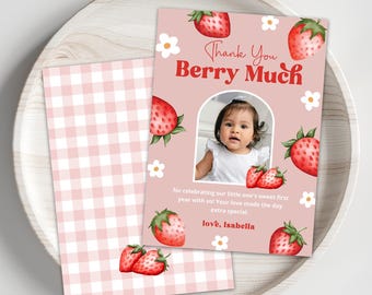 May include: Pink and white gingham thank you card with a photo of a baby girl in a white dress. The card has a strawberry theme with red strawberries and white flowers. The text on the card reads "Thank You Berry Much" and "love, Isabella".
