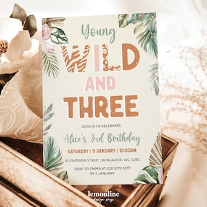 May include: A jungle-themed birthday invitation for a 3-year-old girl. The invitation features a watercolor illustration of tropical leaves and the text "Young Wild and Three" in brown and pink letters. The text "Alice's 3rd Birthday" is also included, along with the date and time of the party.