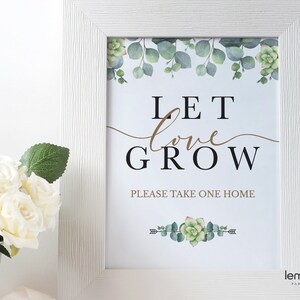 May include: White framed sign with a green and gold floral design. The sign says "Let love grow" and "Please take one home".