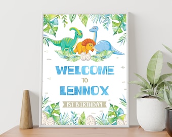 Op de afbeelding: Welkom op Lennox' 1e verjaardag bord met een blauw, groen en geel dinosaurus thema. Het bord toont een blauwe dinosaurus, een groene dinosaurus en een gele dinosaurus met een blauw ei.