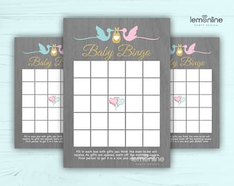 May include: Three gray wood-grain baby shower bingo cards with a blue and pink stork carrying a baby gift box on each card. The text "Baby Bingo" is written in gold glitter letters on each card. The cards are for a baby shower game where guests mark off squares as gifts are opened.