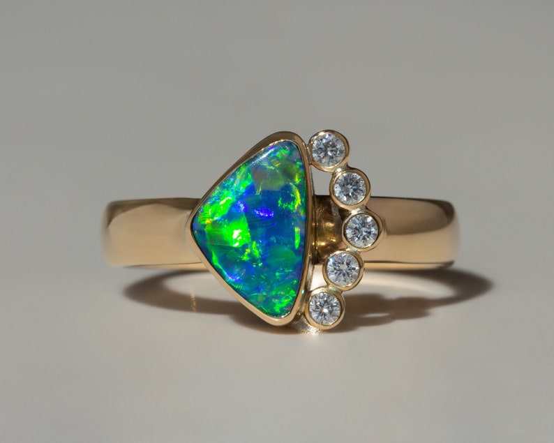 May include: A gold ring with a triangular green and blue opal gemstone and a row of small diamonds on the side.