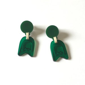 May include: A pair of green acrylic earrings with a rounded top and a teardrop-shaped bottom. The earrings have a subtle, textured design.
