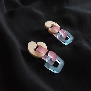 Könnte beinhalten: Ein Paar Statement-Ohrringe mit einem Kettenglied-Design. Die Glieder sind aus durchsichtigem Kunststoff in den Farben Beige, Rosa und Hellblau.