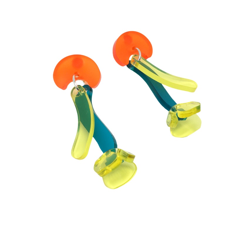Puede incluir: Un par de pendientes de color naranja brillante, amarillo y turquesa. Los pendientes est&aacute;n hechos de acr&iacute;lico y tienen una forma geom&eacute;trica.