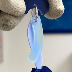 Puede incluir: Un pendiente de acr&iacute;lico azul y morado con forma curva. El pendiente cuelga de un aro plateado.