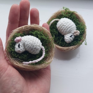 Puede incluir: Dos ratones de ganchillo hechos a mano en nidos en miniatura. Los ratones blancos tienen colas y orejas rosas y están metidos en musgo verde dentro de pequeños nidos tejidos. Un ratón tiene un lazo rosa. Una artesanía encantadora y caprichosa.