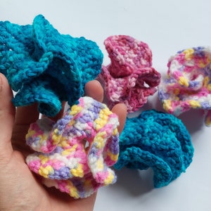 May include: Five crocheted scrubbers in various colors, including pink, blue, and white. The scrubbers are made with a textured, ruffled design.