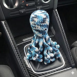 May include: A blue, white, and black crocheted octopus shift knob cover. The octopus design has a round head and multiple tentacles, providing a unique and whimsical touch to a car's interior.