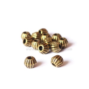 May include: A group of small, gold-colored metal beads with a ridged design. The beads are arranged in a pile on a white surface.