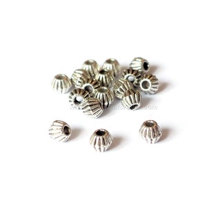 May include: A pile of silver metal beads with a ridged design. The beads have a hole in the center for stringing.
