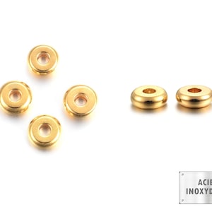 Puede incluir: Cinco cuentas espaciadoras de metal de color dorado, de forma redonda y con un agujero en el centro. Dos cuentas más grandes están en el lado derecho de la imagen, y tres cuentas más pequeñas están en el lado izquierdo. El texto "ACIER INOXYDABLE" está sobre un fondo plateado en la esquina inferior derecha de la imagen.