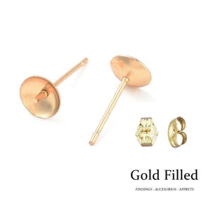 Könnte beinhalten: Vergoldete Ohrstecker mit flachen Pads und passenden Ohrringverschlüssen. Das Bild zeigt zwei Stecker, einen Schmetterlingsverschluss und einen Steckverschluss. Der Text "Gold Filled" ist darunter abgebildet.