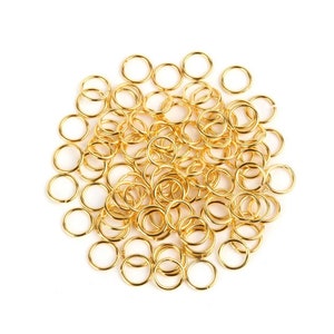 May include: A large pile of gold jump rings. The rings are all the same size and are arranged in a random pattern.