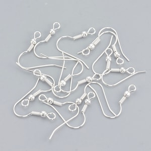 Puede incluir: Primer plano de un grupo de ganchos para pendientes de plata. Los ganchos son de metal y tienen una pequeña bola en la parte superior. Están diseñados para hacer pendientes.