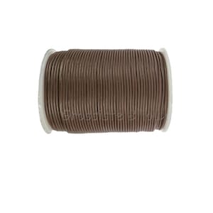 Puede incluir: Un carrete de cordón de cuero marrón, enrollado alrededor de una bobina de plástico blanco.