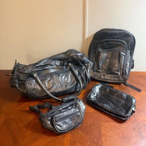 May include: A set of four black leather bags consisting of a large duffel bag with dual handles, a backpack with multiple zippered compartments, a waist bag with an adjustable strap, and a rectangular pouch, all featuring a patchwork design.
