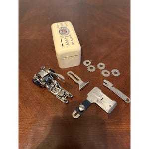 May include: A vintage Singer sewing machine attachment set including a cream-colored plastic storage box with the Singer logo and Made in Switzerland text, a metal presser foot, four small metal cams, and two additional metal sewing components.