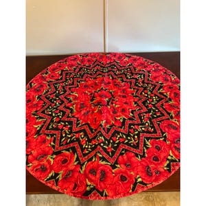 May include: A circular fabric mat featuring a vibrant red poppy floral pattern set against a deep black background. The design incorporates a geometric star-shaped motif radiating from the center, surrounded by detailed red poppy blossoms.