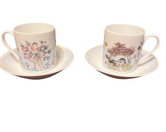 May include: Two white porcelain teacups and saucers with floral and bird designs. The cups feature a blue and white floral pattern with a bird perched on a branch. The saucers have a blue and white floral border.